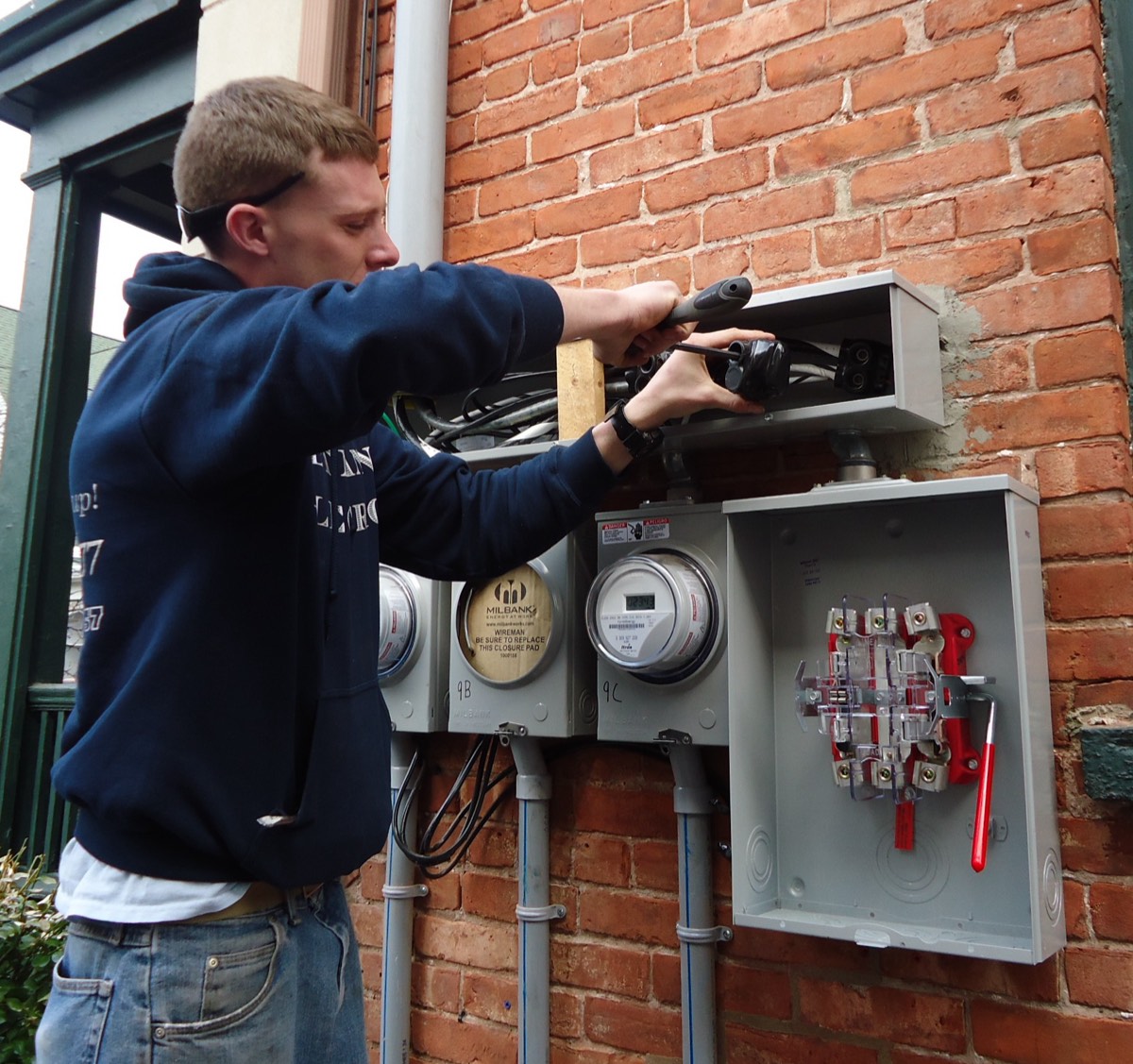 Electrician working on exterior electrical service panels at a home